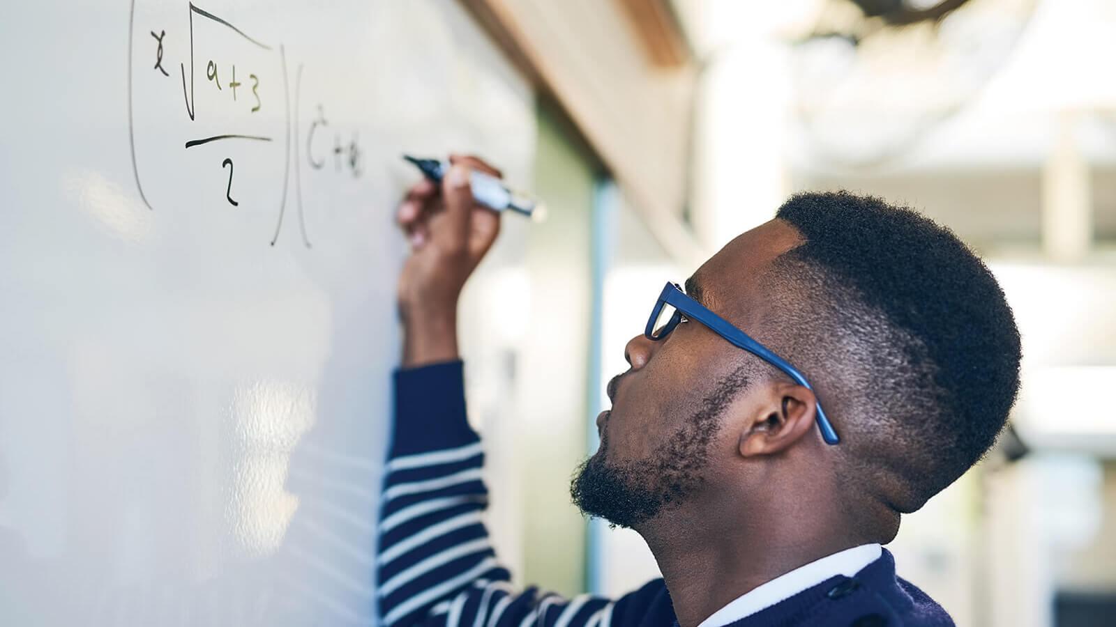 Black male student with glasses working on math equation at whiteboard
