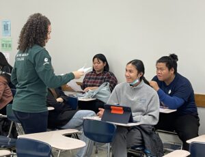 Coach handing out papers and chatting with three students in a classroom setting