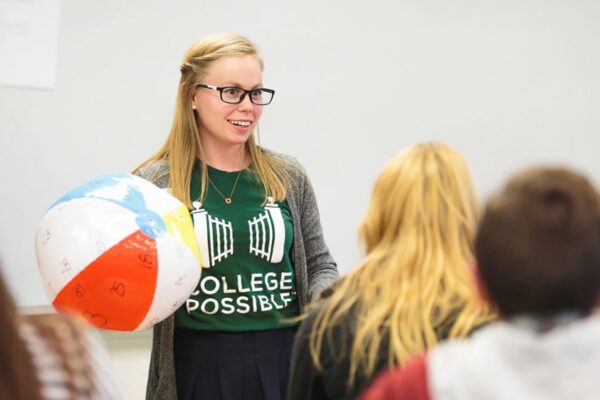 A College Possible AmeriCorps Coach Stands At The Front Of A Classroom Holding A Beach Ball As She Leads Students In An Activity.