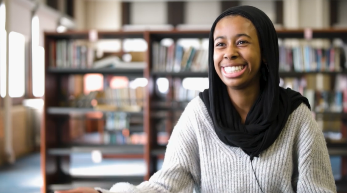 Video screenshot of student smiling in a library