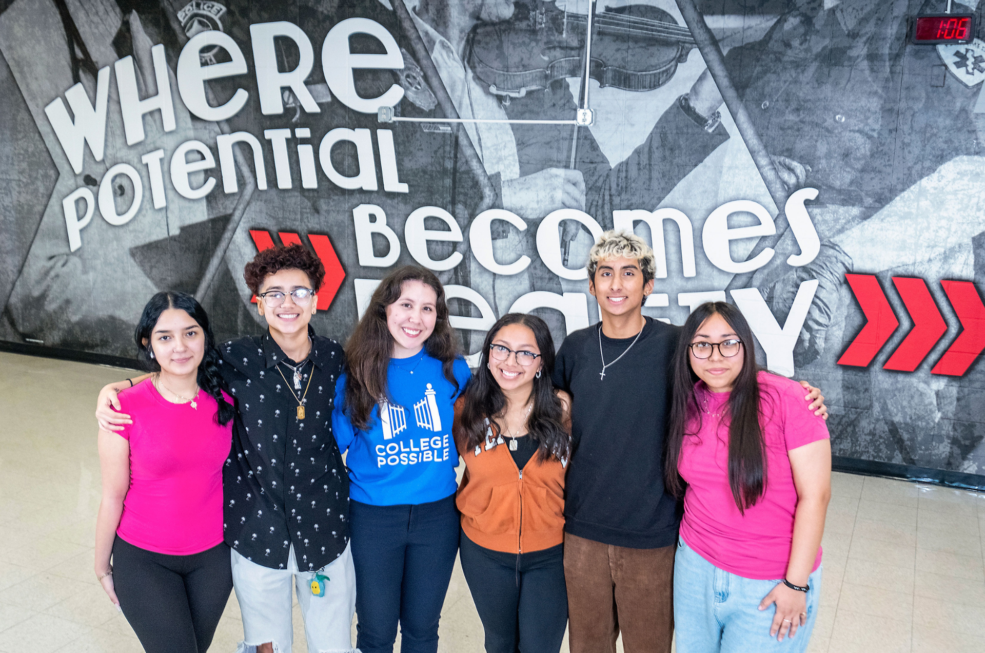 n AmeriCorps coach stands in front of a mural with the words “Where potential becomes reality” alongside five College Possible students.