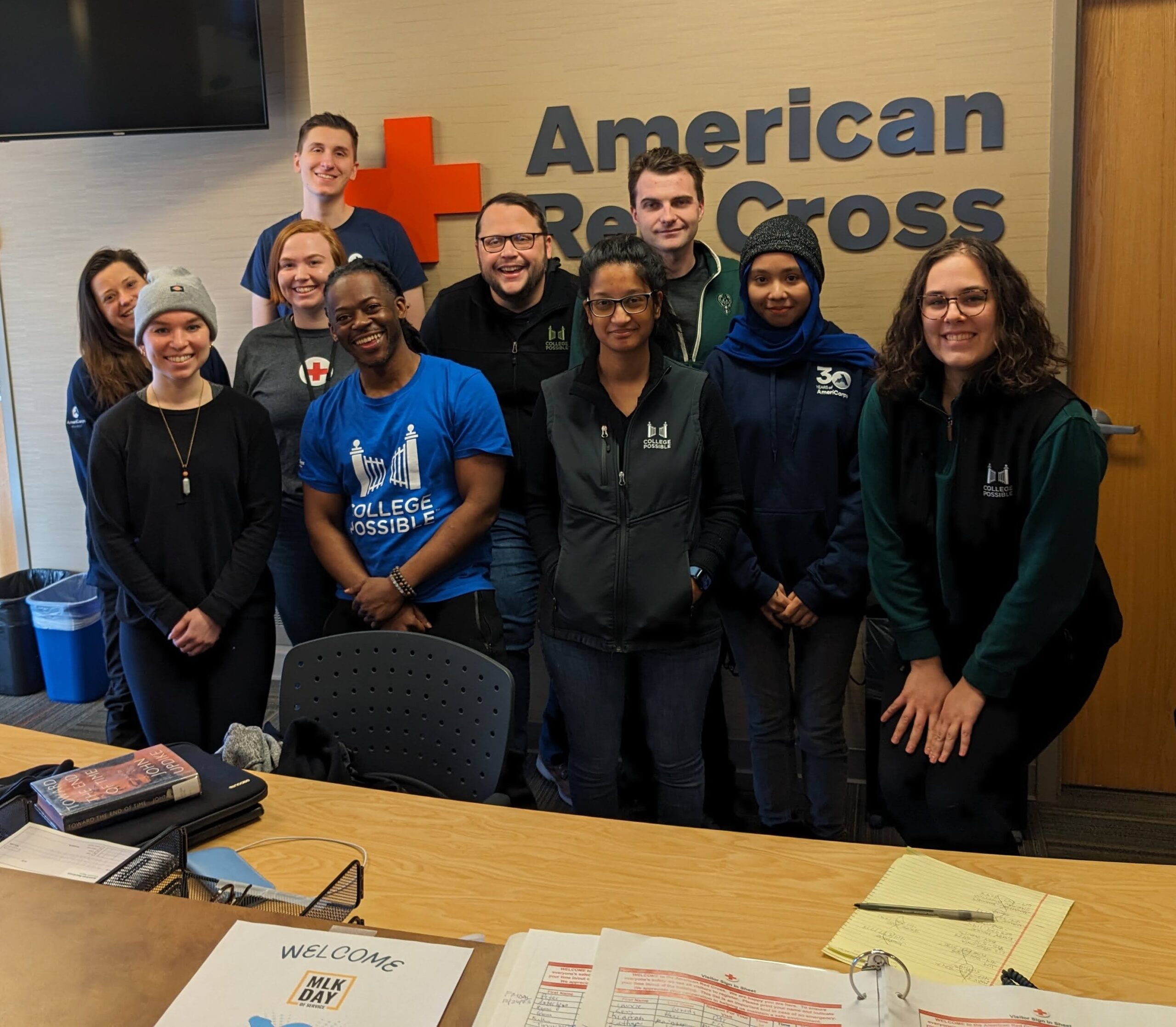 A group of eight smiling College Possible team members wearing College Possible gear standing in front of an American Red Cross sign.