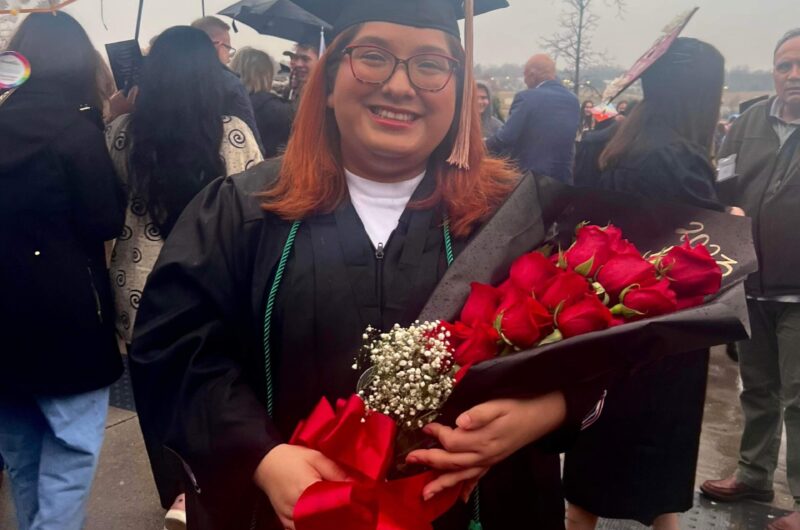 Photo Of Lessly At Graduation In Her Cap And Gown Holding A Flower Bouquet.