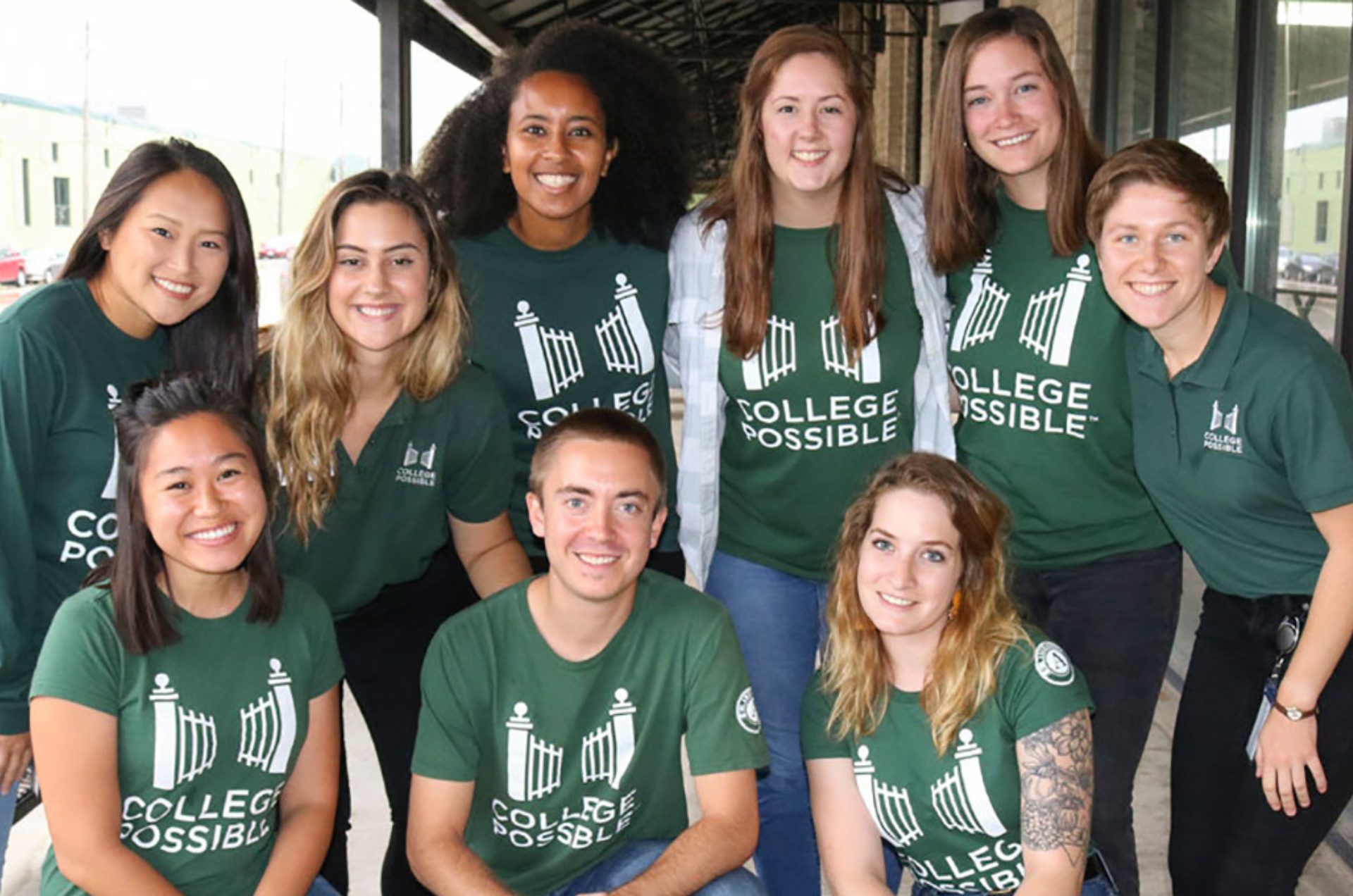 A group of nine coaches smile at the camera in their green AmeriCorps College Possible shirts