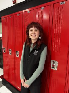 Photo of Missy wearing a College Possible vest and standing in front of red lockers