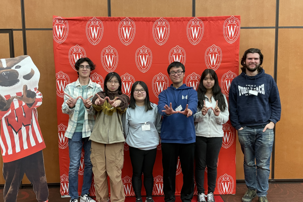 Photo Of 5 Students And A College Possible Coach Making A “W” Hand Sign For Wisconsin In Front Of A Red UW-Madison Backdrop.