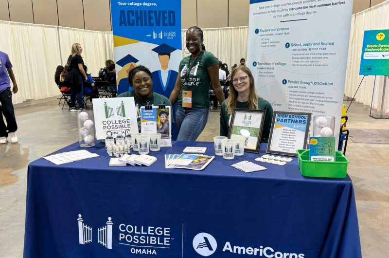Photo Of The College Access Team Behind Their Event Table Set Up With College Possible Swag. From Left To Right: Darrien Seated Behind The Table, Aminatu Standing Centered Behind The Table, Christina Seated Behind The Table.