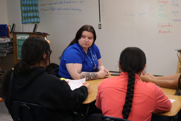 Photo Of Coach Bre Sitting At Desk Assisting Students.