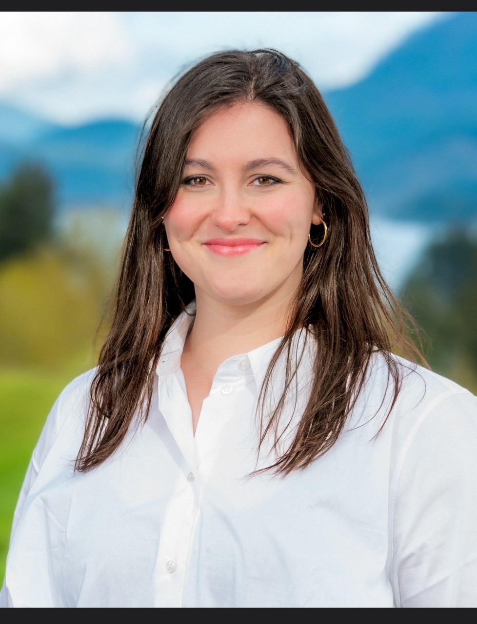 Woman in white shirt stands in front of mountain & river background