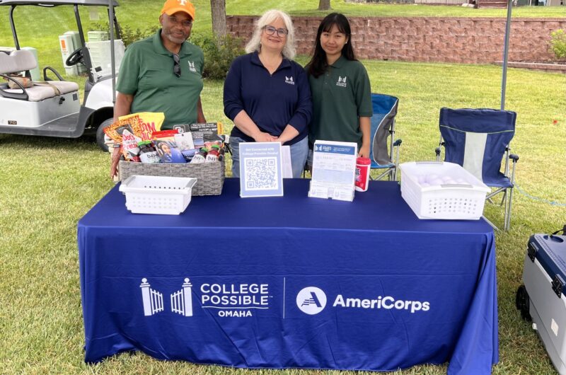 Photo Of Ruth Standing Behind A College Possible Table With Melissa Robinson And Arvin Frazier At The La Vista Community Foundation Golf Tournament.