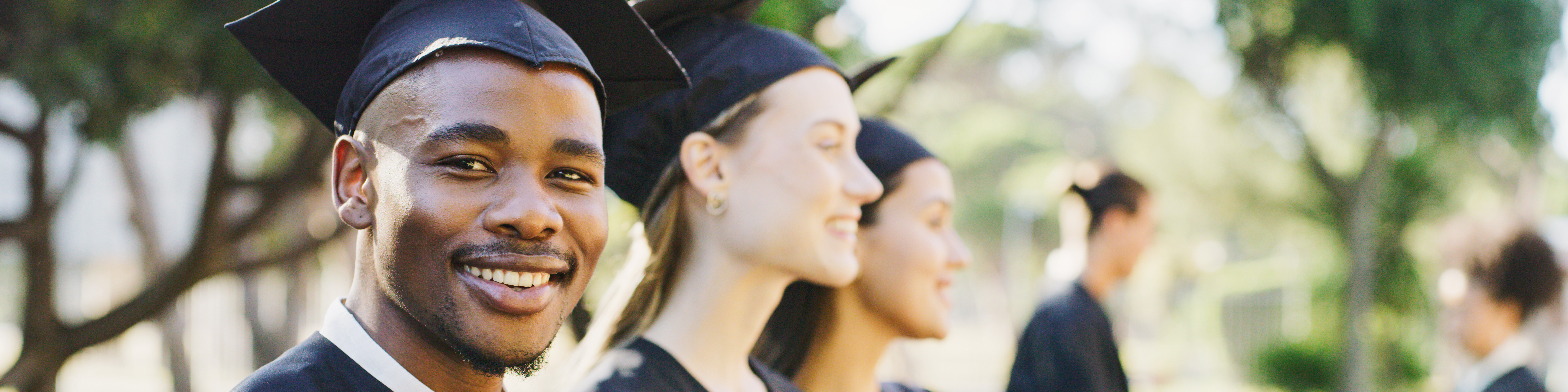 A group of college graduates smile while standing outside.