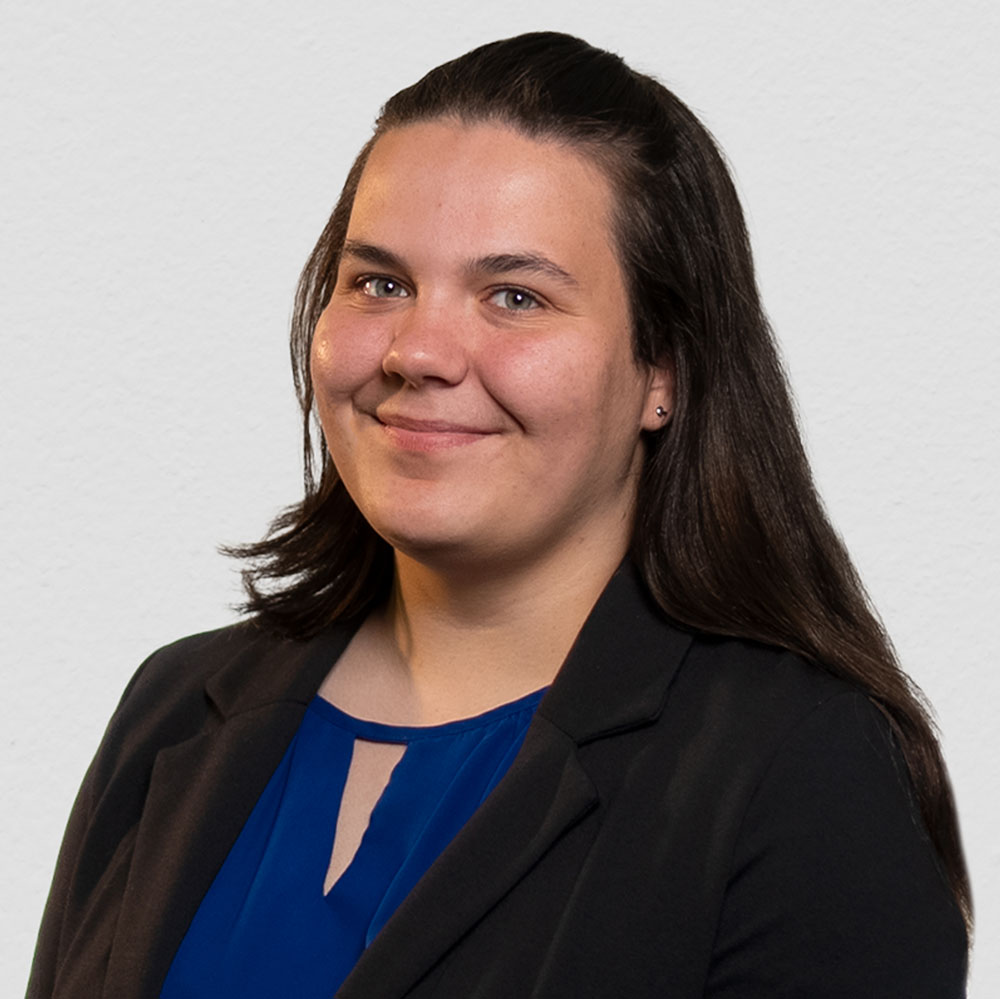 Young person in a blue blouse and black blazer jacket stands in front of a white background