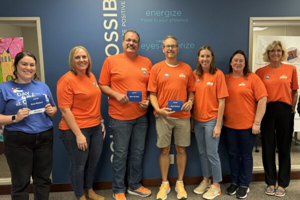 Volunteers From Omaha Public Power District And A United Way Representative Standing Together Smiling, Holding The “Best Wishes” Cards They Wrote To Students.