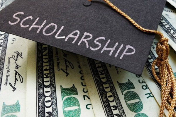 Graduation Cap With "scholarship" Written On It Laying On Top Of Layered $100 Bills.