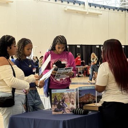 Three Individuals Are Attentively Reading Brochures At A College Fair Booth Staffed By A Representative. The Booth Features Various Informational Materials And A Banner Of Rutgers University.