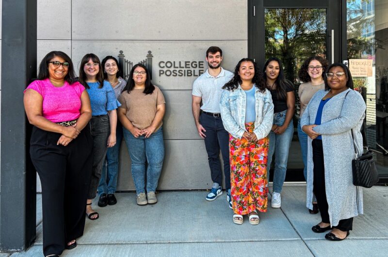 A Group Of Professionals Pose Outside An Office Building With The College Possible Logo On It.