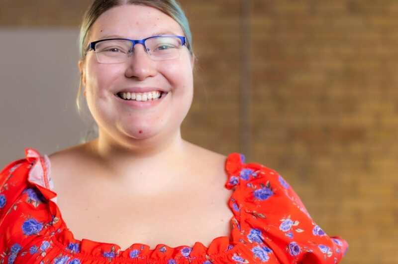 Person In Orange Top Wearing Blue-frame Glasses Smiling