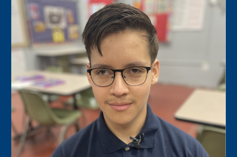 A Male Student Wearing Glasses And A Navy Polo Smiling At The Camera