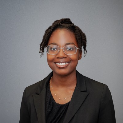 Professional Headshot Photo Of Grace Wearing A Black Blouse, Blazer, And Glasses, Smiling.