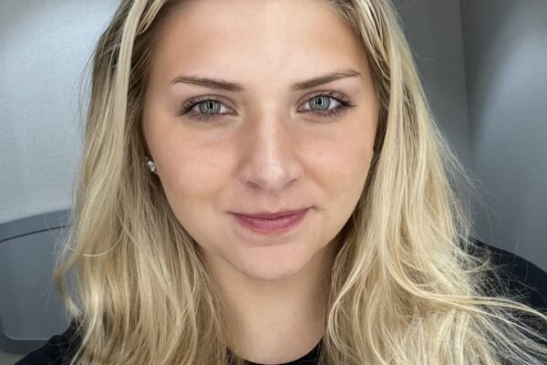 Photo Of Marysue With Long Blonde Hair And A Black Top Smiling Slightly At The Camera In A Well-lit Room.