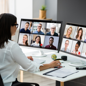 A Person Participates In A Virtual Meeting With Eight Colleagues Displayed On A Large Monitor.