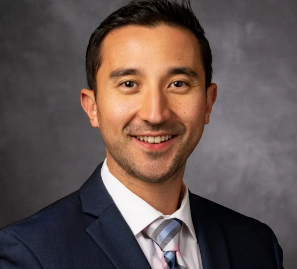 Dr. Jonathan Rowland’s professional headshot. He wears a dark grey suit and striped tie in front of a light gray background.