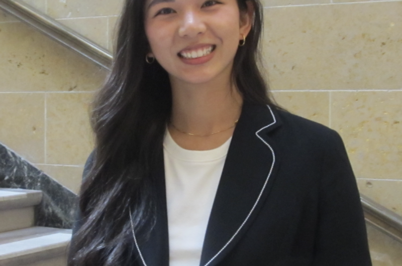 Person smiling in a business suit, standing in front of a marble staircase.