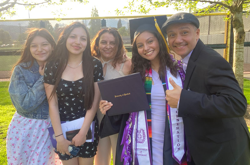 A graduate poses with her family and diploma outside.