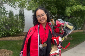 Moolaweh dressed in her graduation regalia and holding a bouquet of flowers, smiling at the camera.