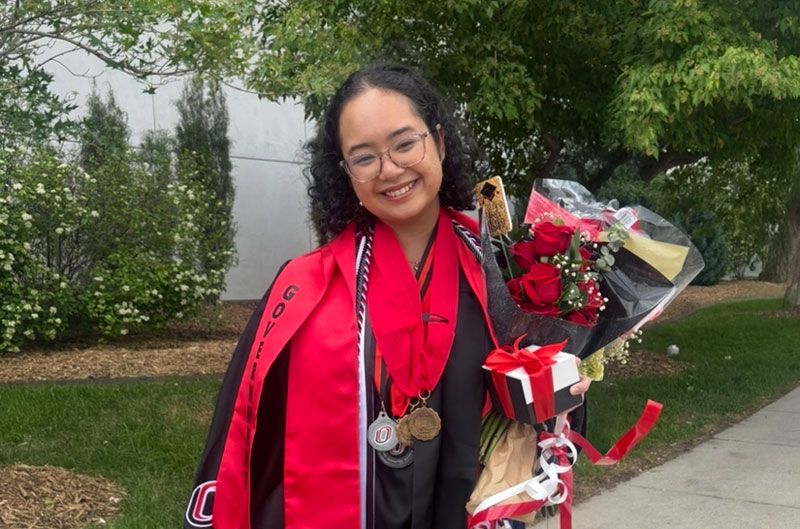 Moolaweh dressed in her graduation regalia and holding a bouquet of flowers, smiling at the camera.
