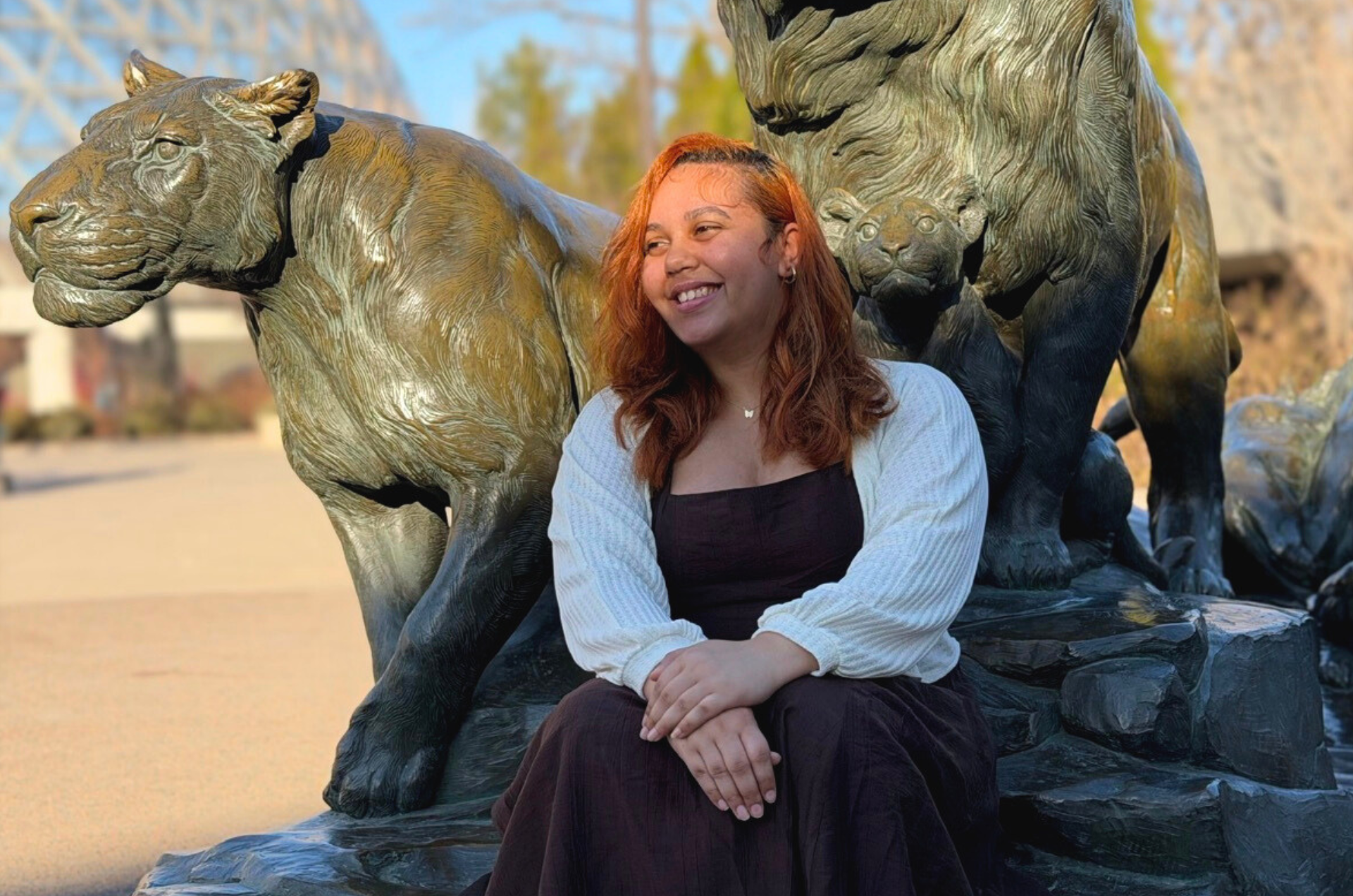 Kendra sits in front of a lion and lioness statue at the Omaha Henry Doorly Zoo with the Desert Dome in the background.