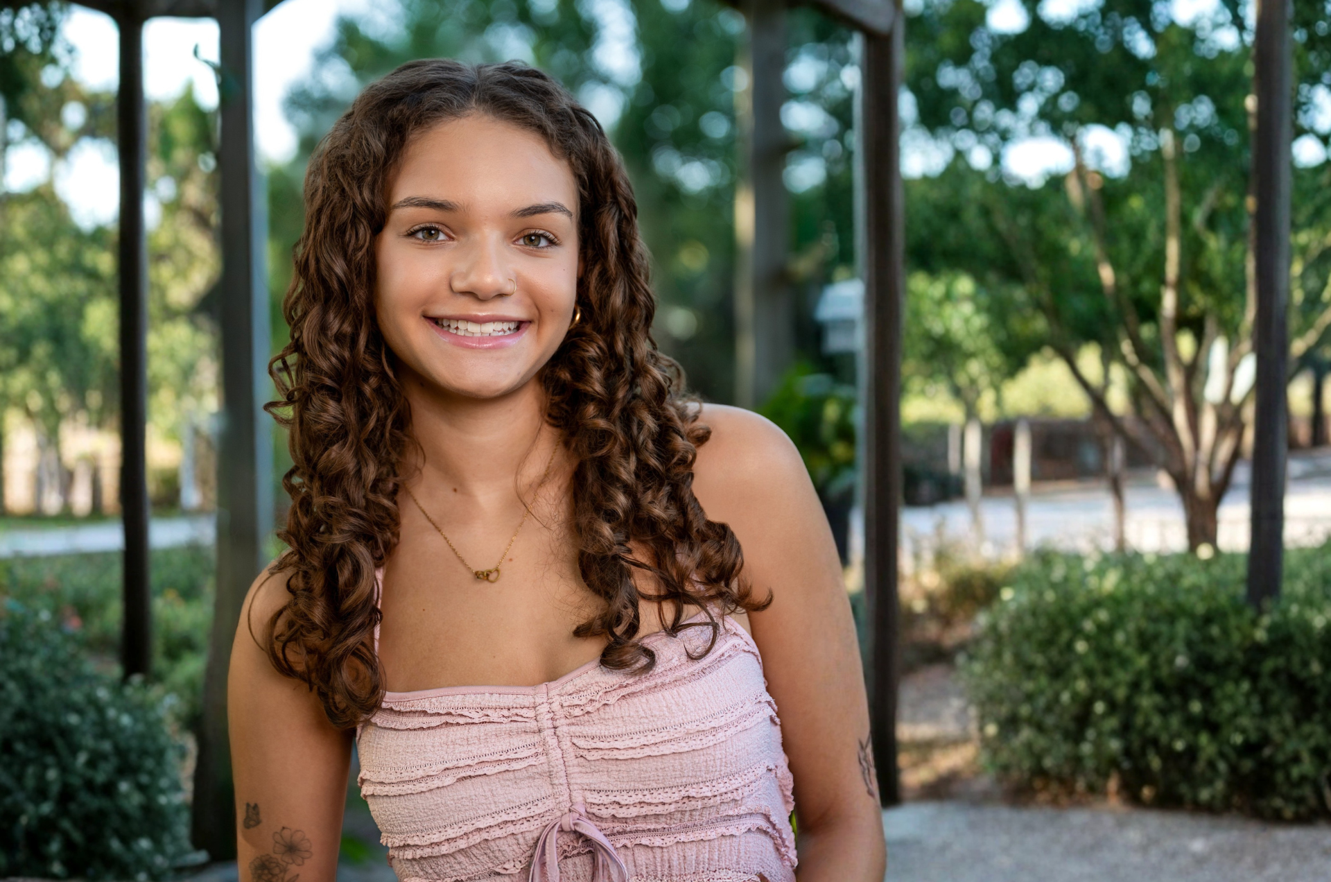 Jaidyn smiles at the camera, wearing a pink textured top, with a blurred natural background.
