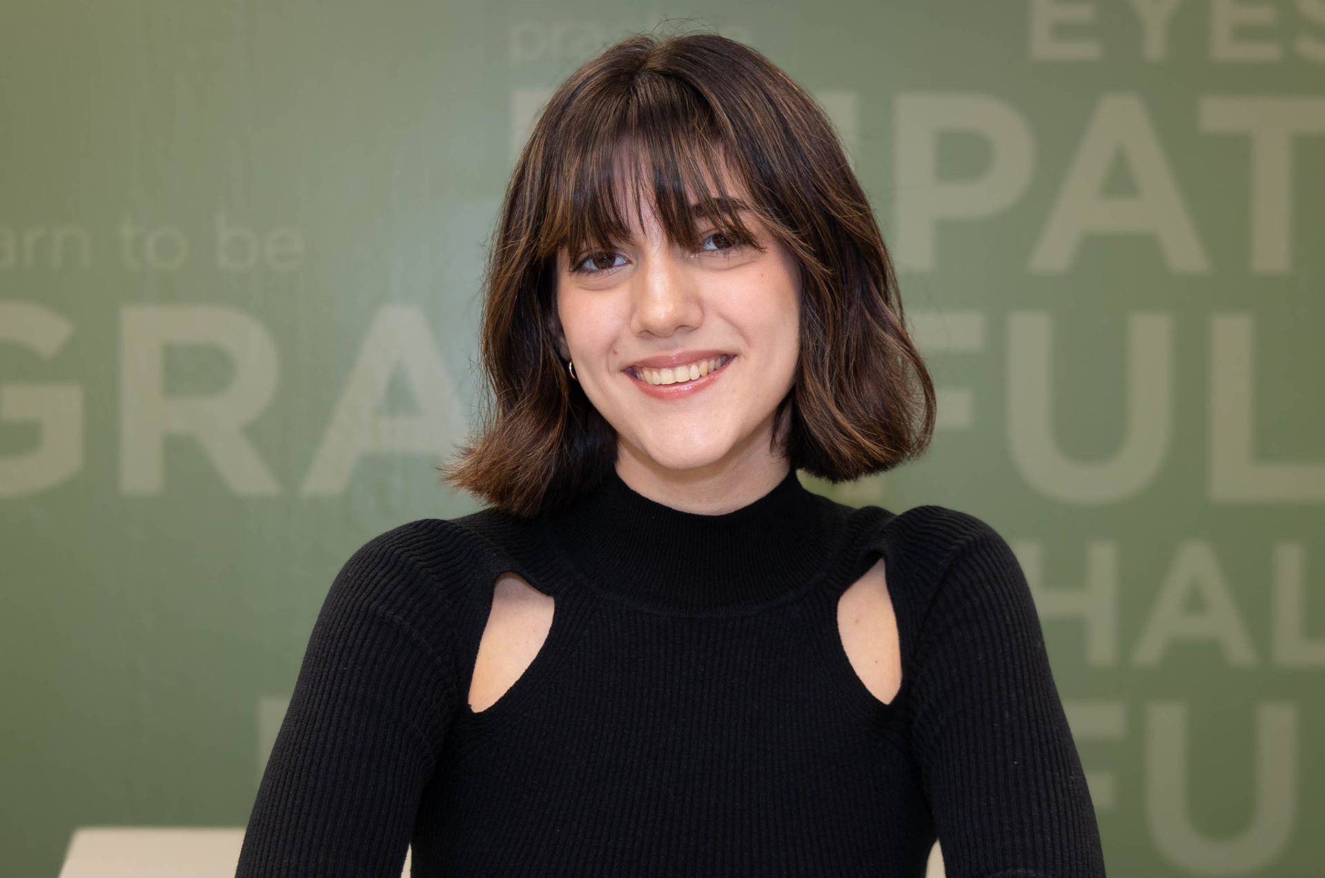 student with short brown hair sitting at table smiling at the camera