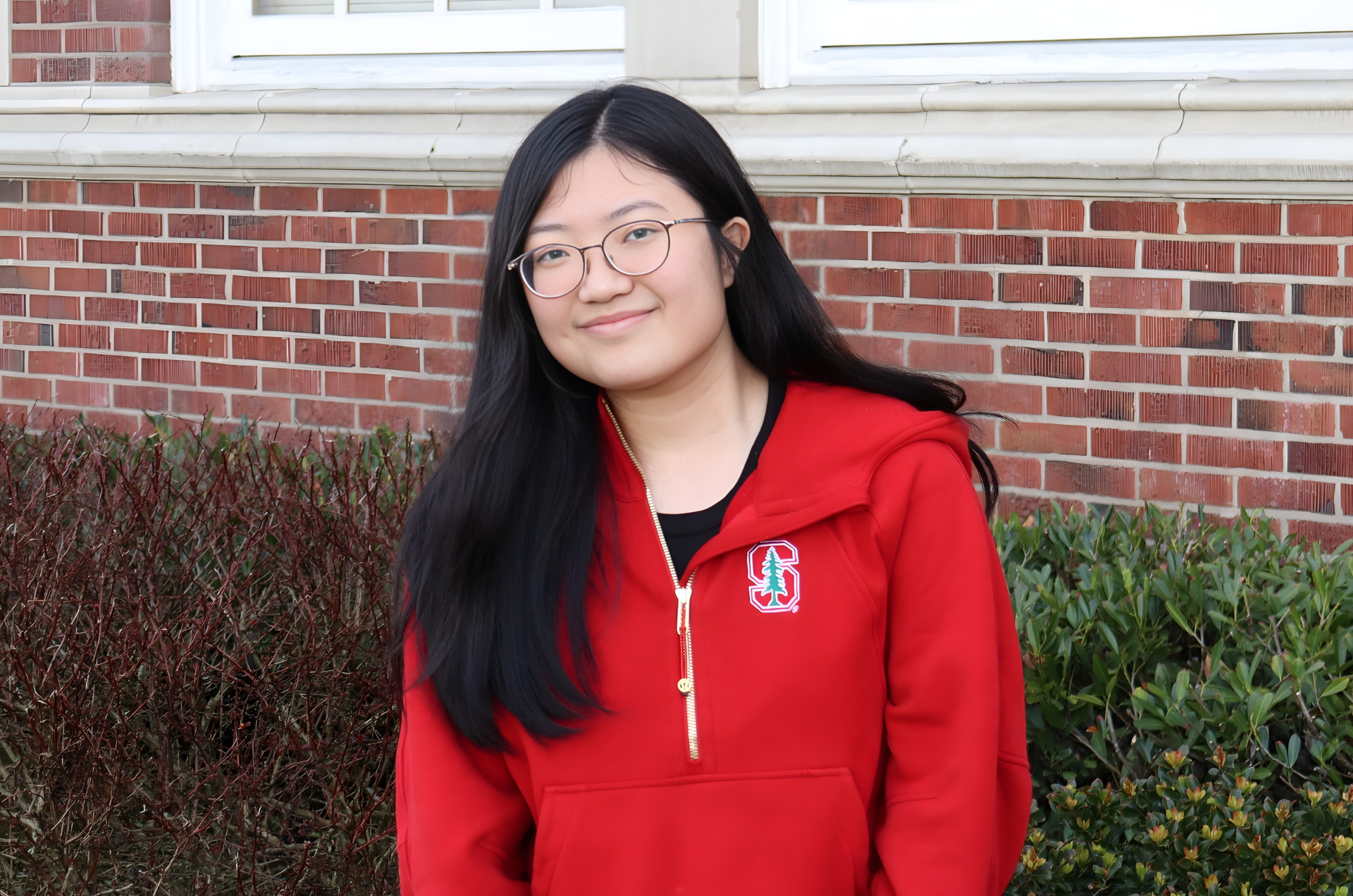 Xintong smiles at the camera, wearing a red Stanford hoodie.