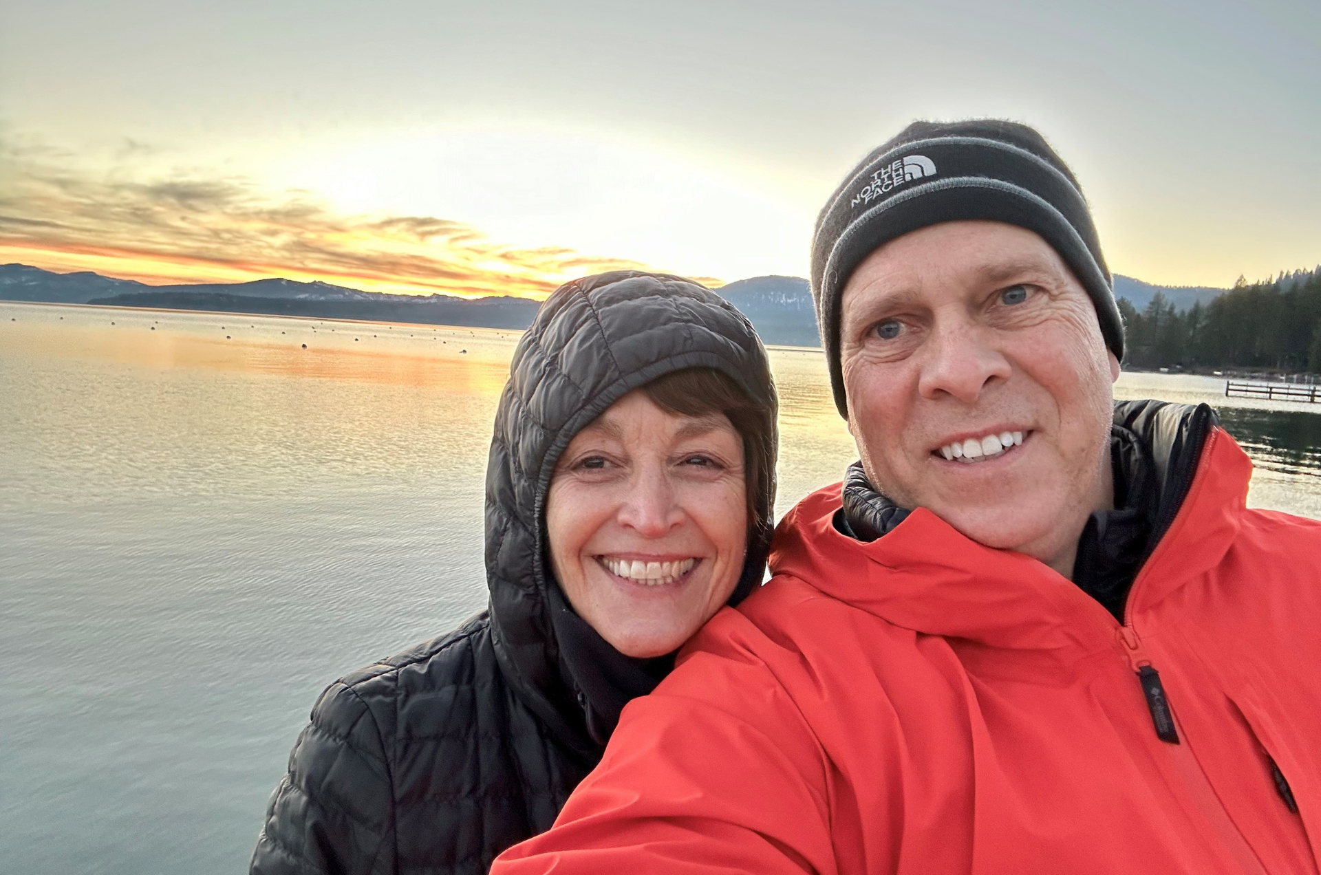 smiling couple taking a selfie in front of water at sunset