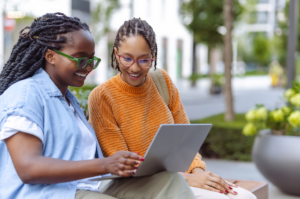 Two female students, both wearing eye glasses, look at a laptop