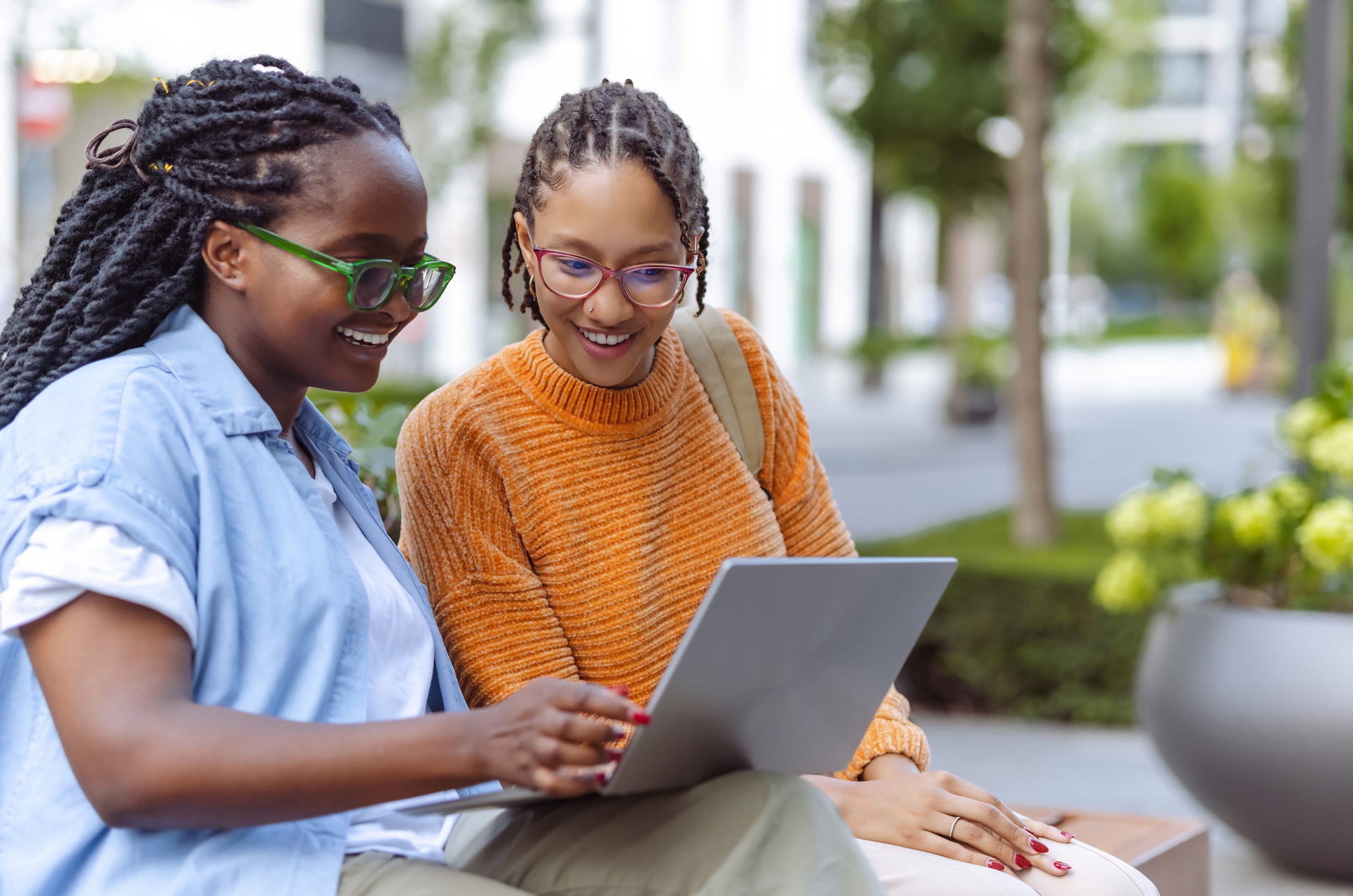 Two female students, both wearing eye glasses, look at a laptop