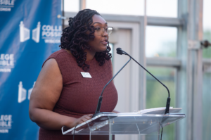 woman dressed in a brown dress speaking at a podium