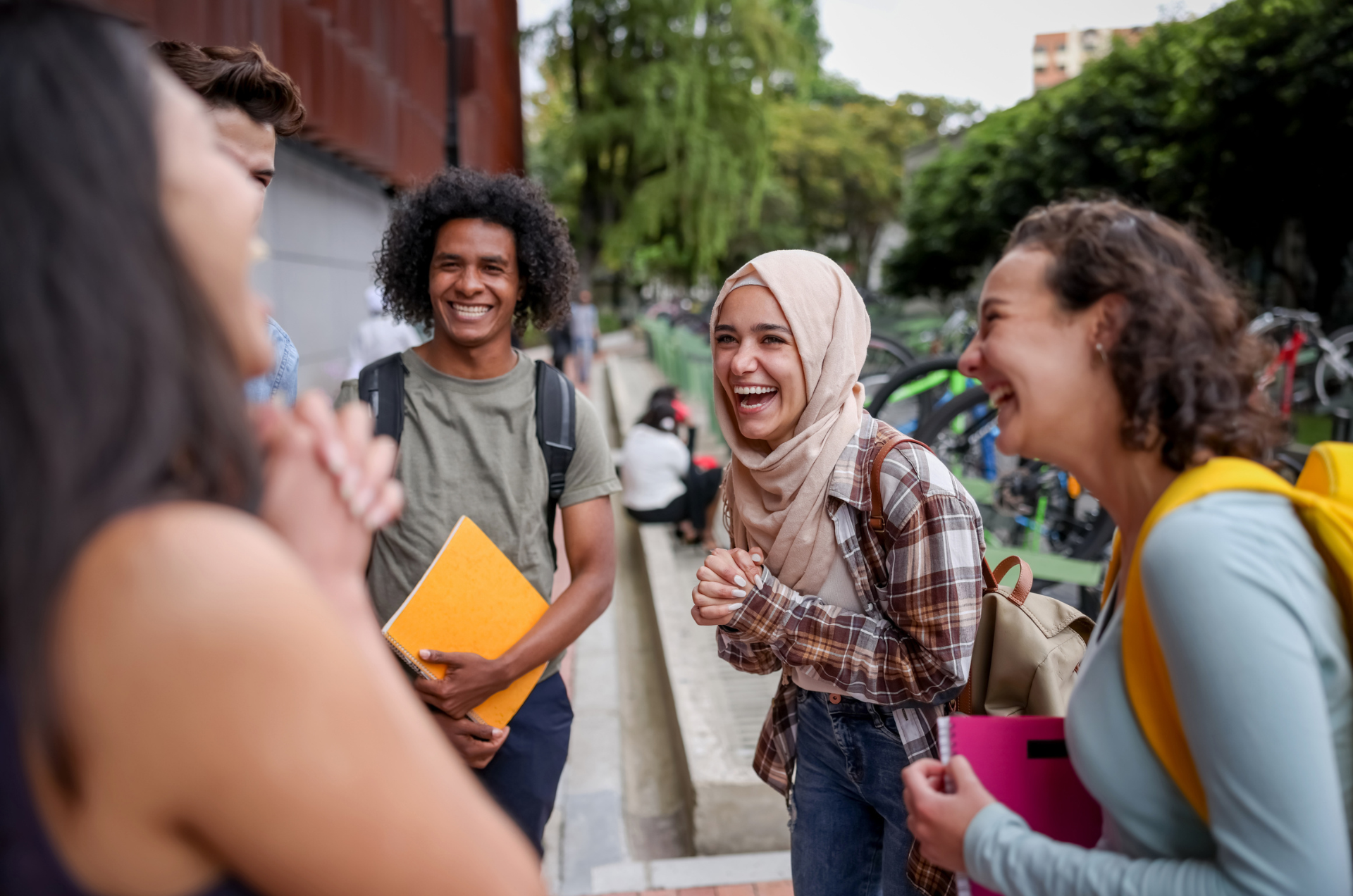 Five college students stand in a circle on the steps of a university campus, laughing and conversing at the start of the school year.