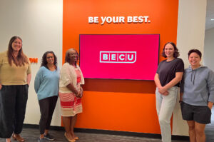 College Possible staff pose together in front of a BECU-branded 'Be Your Best' wall, with Tisha Held pictured among them