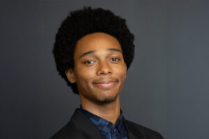 A young man wearing a collared shirt and jacket smiles at the camera.
