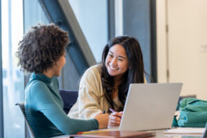 A College Possible coach and her student are sitting over a laptop, smiling while discussing her future.